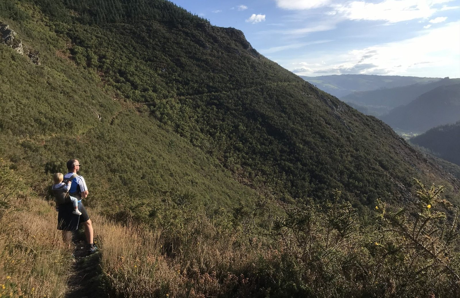 Marcos Losa con su hija a hombros de ruta por la naturaleza en Asturias, mirando al horizonte